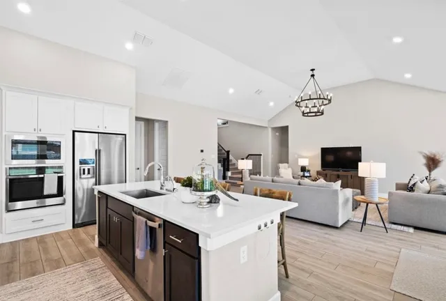 a large kitchen with stainless steel appliances a stove a sink dishwasher a refrigerator and a dining table with wooden floor