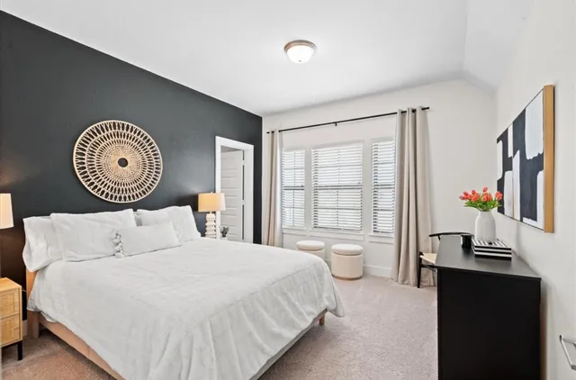a bedroom with a bed and a lamp on dresser with a large window