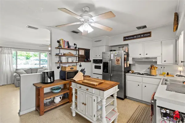 a kitchen with stainless steel appliances a stove a refrigerator a sink a stove and white cabinets with wooden floor