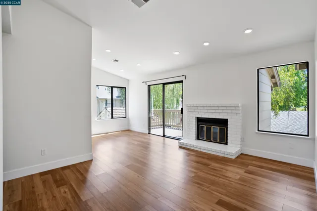 an empty room with wooden floor fireplace and windows