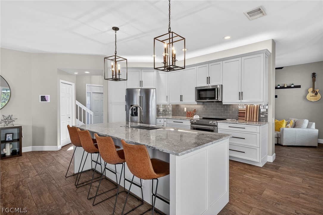 22866 Forest Ridge Drive Estero, FL 33928 - Photo 3 of 38 a kitchen with stainless steel appliances granite countertop a stove top oven a refrigerator a sink a dining table and chairs with wooden floor