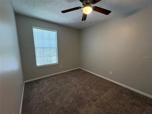 an empty room with a chandelier fan and windows