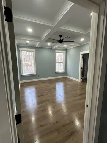 a view of an empty room with wooden floor and a ceiling fan