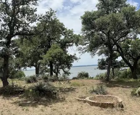 4215 Sunset Cliff Road Burnet, TX 78611 - Photo 7 of 13 An inviting lake view with mature trees and a rustic fire pit for outdoor enjoyment.