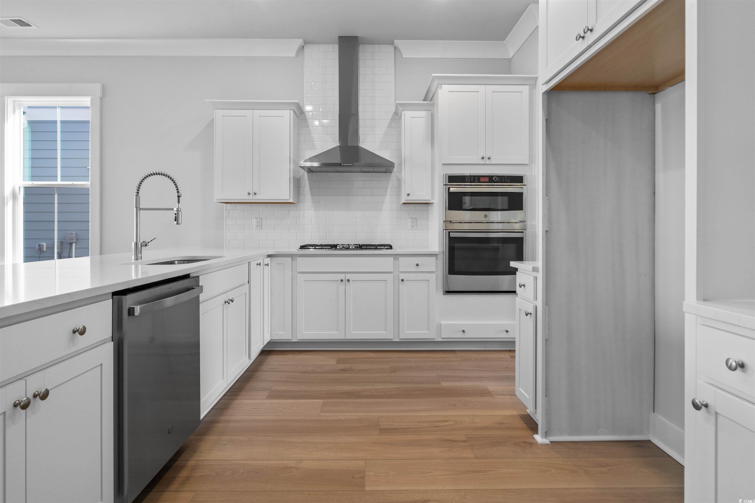 220 Atlantic Breeze Street Myrtle Beach, SC 29572 - Photo 20 of 38 Kitchen featuring white cabinetry, stainless steel appliances, wall chimney exhaust hood, light wood-style floors, and backsplash