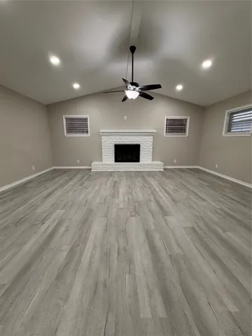 an empty room with wooden floor ceiling fan and windows