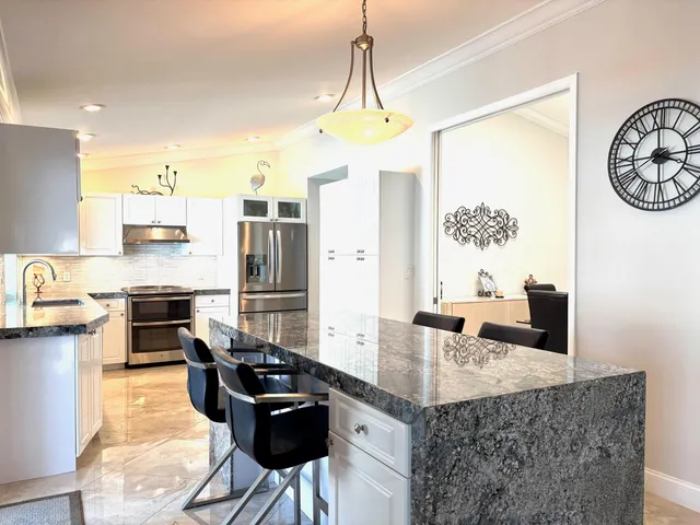 a kitchen with granite countertop a stove a refrigerator a kitchen island a dining table and chairs