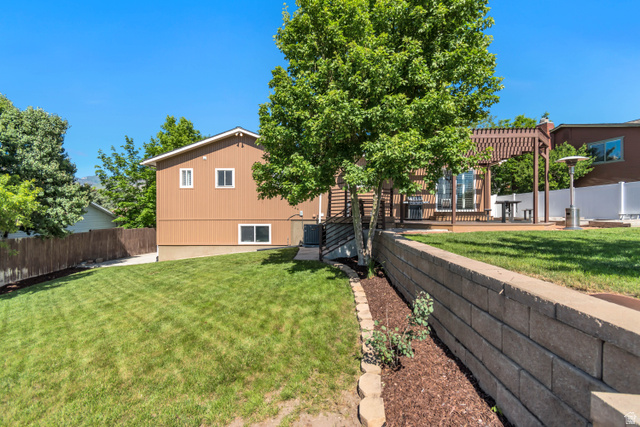 9832 Falconhurst Drive Sandy, UT 84092 - Photo 25 of 29 Private backyard featuring an elevated wood deck with a pergola, a block retaining wall, and mature landscaping