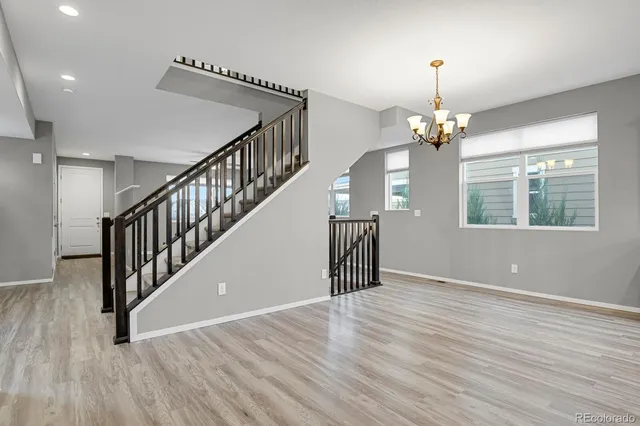 a view of an empty room with wooden floor staircase and a kitchen