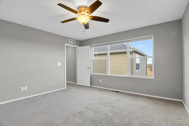 an empty room with chandelier fan and windows