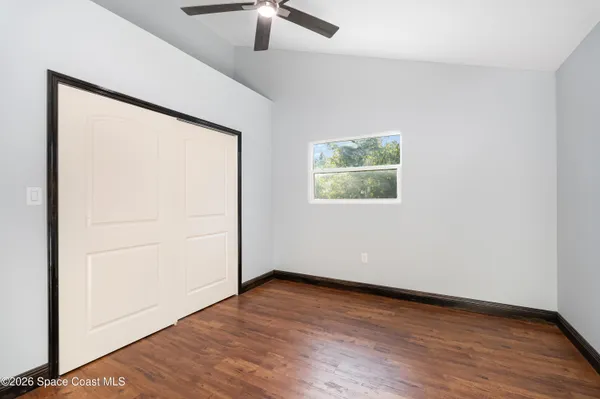 an empty room with wooden floor chandelier fan and windows