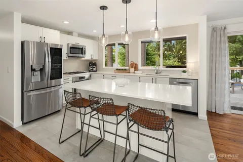 a kitchen with stainless steel appliances a stove a sink a microwave a refrigerator and white cabinets with wooden floor