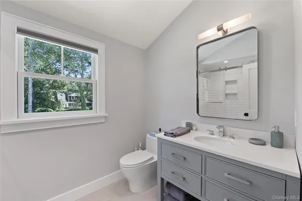 a bathroom with a granite countertop toilet a sink a mirror and a window
