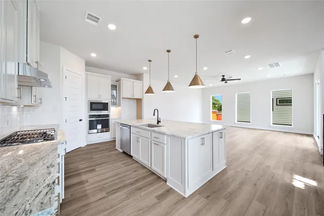 a kitchen with stainless steel appliances granite countertop a sink a stove and a wooden floor