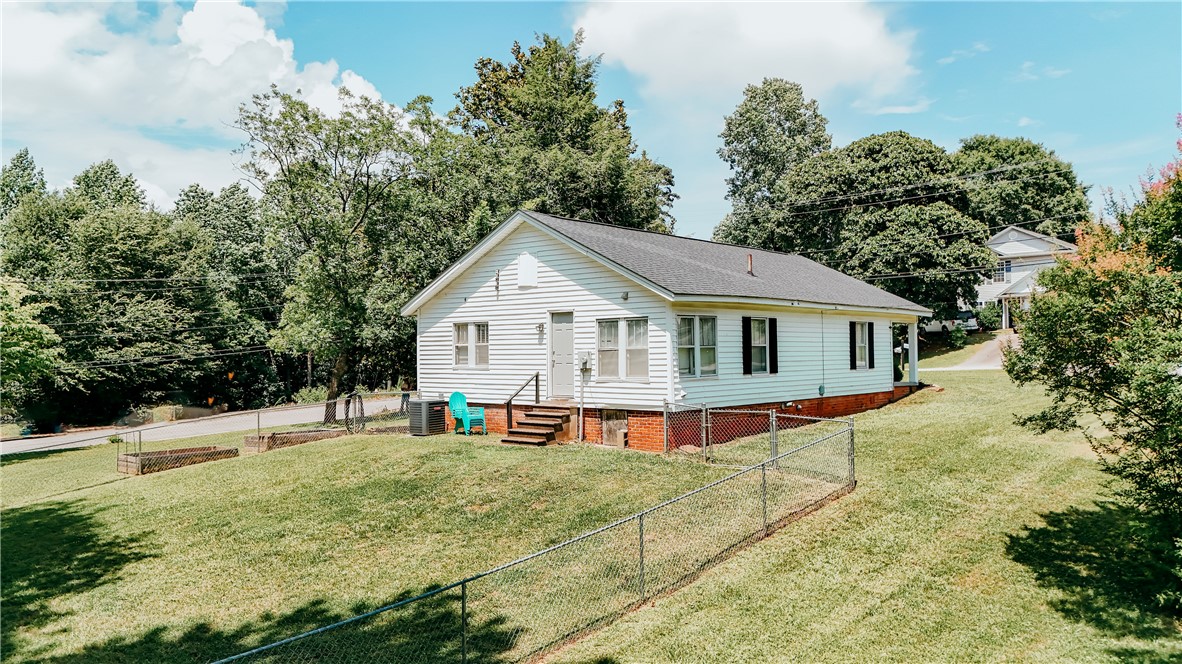 310 North Chestnut Street Seneca, SC 29678 - Photo 11 of 30 A charming single-story residence with classic siding, offering a serene backdrop of mature trees and a gently sloped yard.