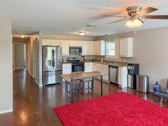 a kitchen with stainless steel appliances kitchen island granite countertop a dining table chairs refrigerator and sink
