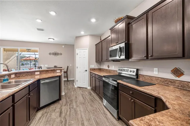 a kitchen with stainless steel appliances granite countertop wooden cabinets a sink dishwasher a stove and a refrigerator with wooden floor