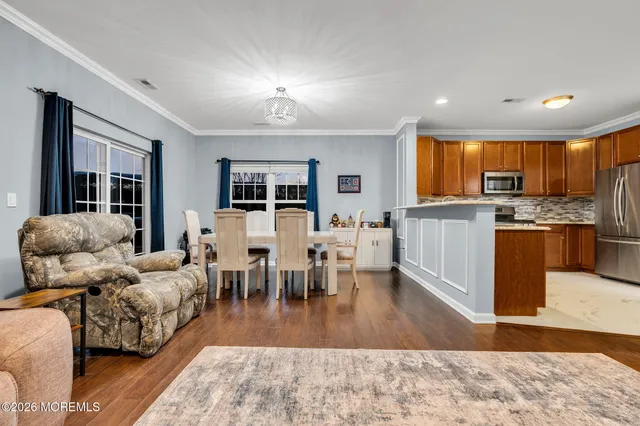 a living room with stainless steel appliances furniture wooden floor and a kitchen view