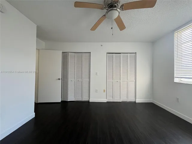 an empty room with wooden floor ceiling fan and windows