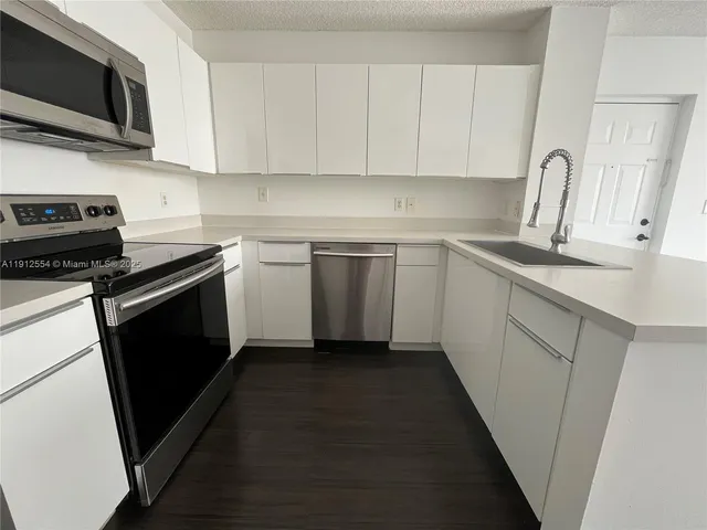 a kitchen with stainless steel appliances a sink dishwasher a stove top oven a refrigerator with grey cabinets and wooden floor