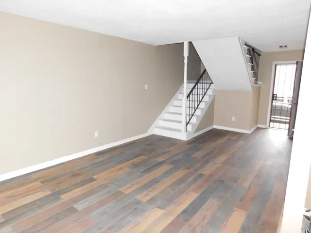 a view of an empty room with wooden floor and stairs