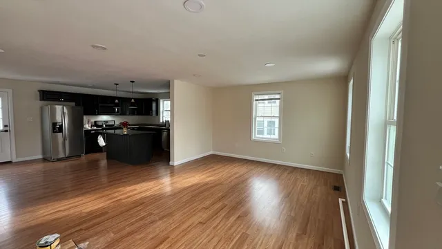 an empty room with wooden floor kitchen view and a window