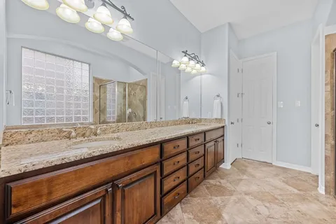 a spacious bathroom with a granite countertop double vanity sink a mirror and a shower