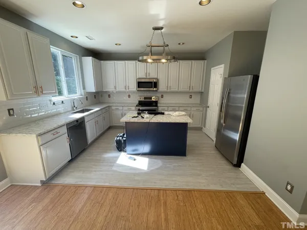 a large kitchen with stainless steel appliances a stove a sink dishwasher a refrigerator and a oven with wooden floor