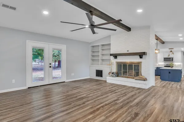 a view of a room with wooden floor a fireplace a ceiling fan and windows