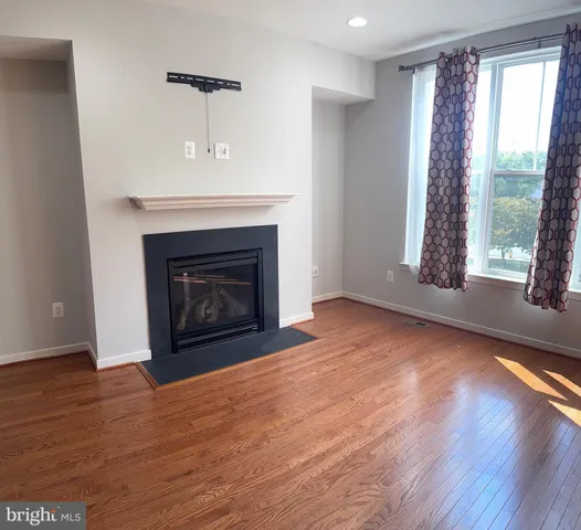 a view of an empty room with wooden floor fireplace and a window
