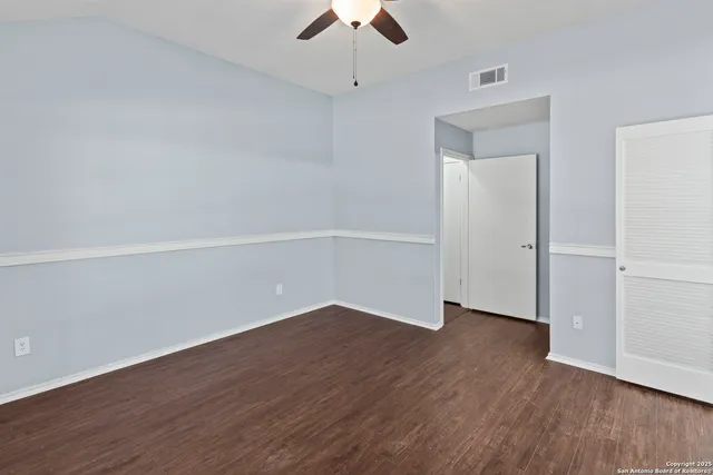 an empty room with wooden floor chandelier fan and windows