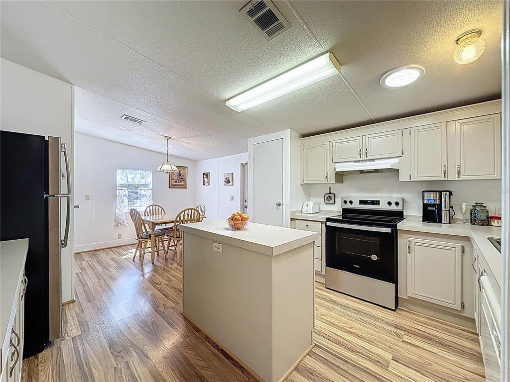 251 Patterson Road, Unit I3 Haines City, FL 33844 - Photo 4 of 38 a kitchen with stainless steel appliances a stove top oven a refrigerator a dining table and chairs with wooden floor