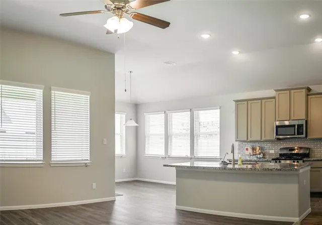 a kitchen with granite countertop a stove a sink a refrigerator and white cabinets with wooden floor