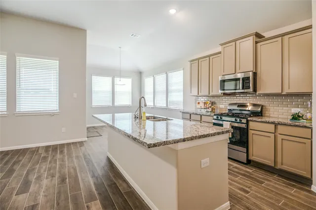 a kitchen with stainless steel appliances granite countertop a stove a sink dishwasher a refrigerator and a microwave oven with wooden floor