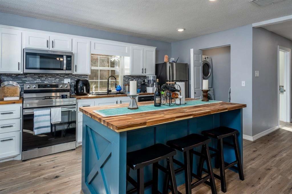 365 Co Road Stamford, TX 79553 - Photo 4 of 23 Kitchen featuring a central island with wood-finish countertop, white cabinetry with dark hardware, stainless steel appliances, and wood-finish flooring