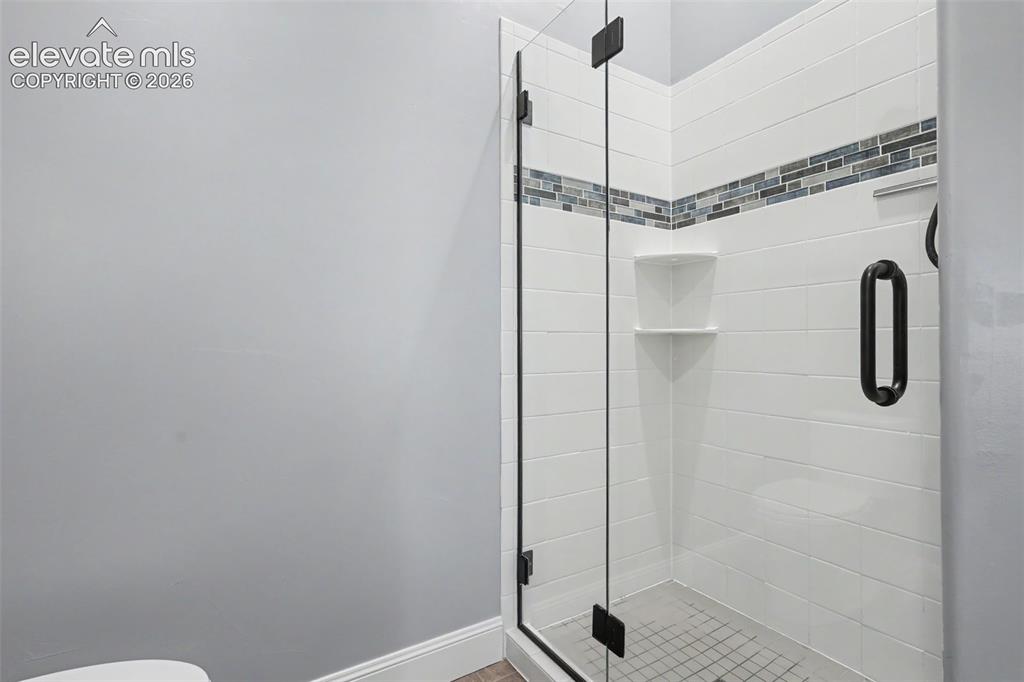21 Leaming Road Colorado Springs, CO 80906 - Photo 36 of 48 Walk-in shower featuring a clear glass enclosure with matte black hardware, white subway tile surround with a mosaic accent band, and integrated corner shelving