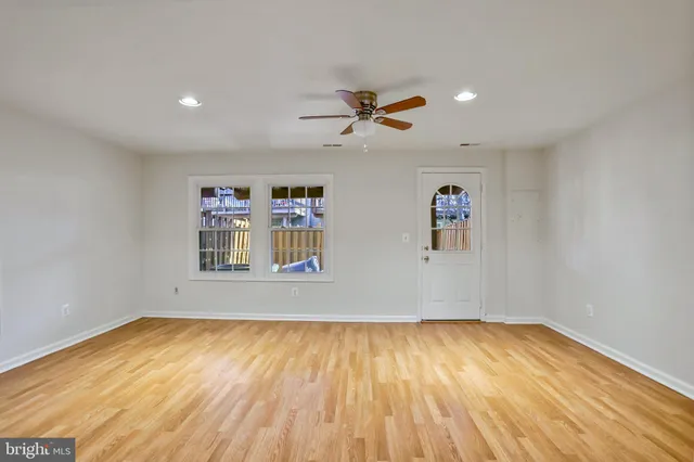 a view of an empty room with wooden floor and a ceiling fan