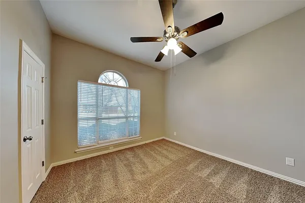 an empty room with a chandelier fan and windows