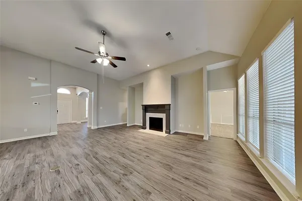 an empty room with large windows a fireplace a ceiling fan and wooden floor
