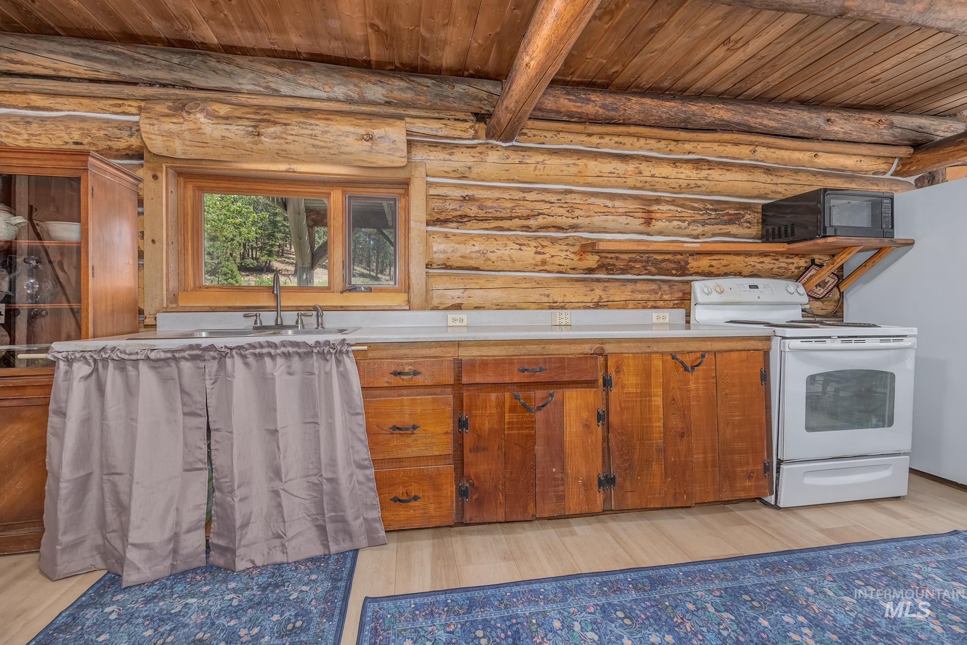 2150 Seid Creek Road Cambridge, ID 83610 - Photo 7 of 50 Rustic kitchen featuring natural log walls, wood-finish flooring, a wood-framed window, wooden cabinetry, and light countertops