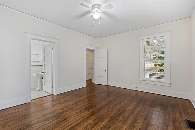 an empty room with wooden floor chandelier fan and windows