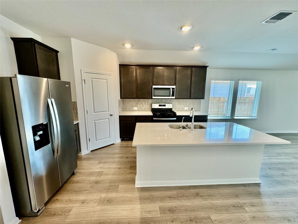 141 Boondoggle Ridge Cedar Creek, TX 78612 - Photo 2 of 7 Kitchen with stainless steel appliances, dark brown cabinets, a center island with sink, light stone countertops, and backsplash
