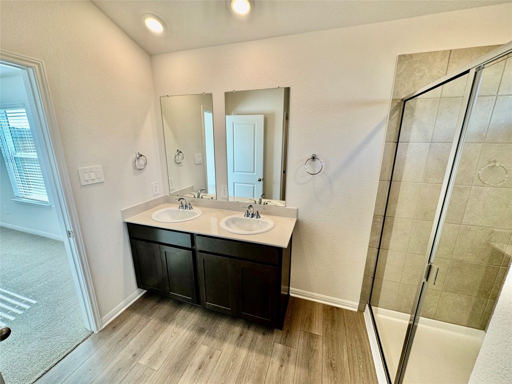 141 Boondoggle Ridge Cedar Creek, TX 78612 - Photo 4 of 7 Bathroom featuring double vanity, a stall shower, light wood-style floors, and a textured wall