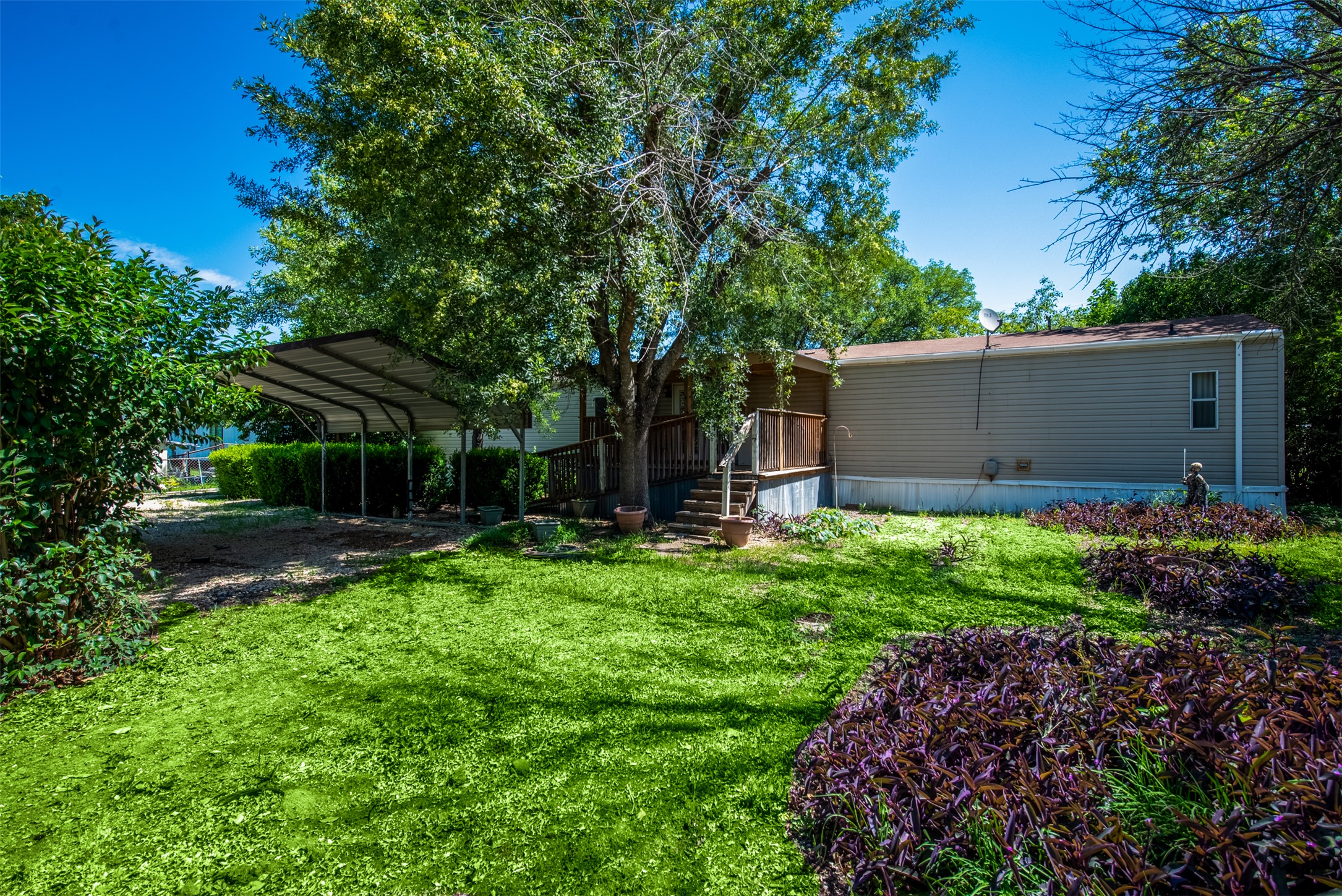 258 Quail Ridge Drive Kyle, TX 78640 - Photo 10 of 11 Manicured lawn with mature trees, a metal carport, a wooden deck with stairs, and a property with horizontal siding