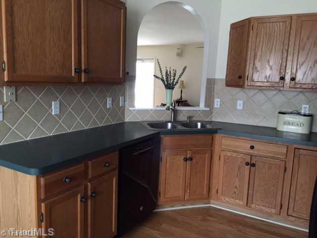 7602 Keating Drive Oak Ridge, NC 27310 - Photo 5 of 18 Kitchen. Delightful kitchen has oak cabinetry, tile backsplash double SS sink, black DW/flattop range-oven/built-in microwave and overlooks the LR.