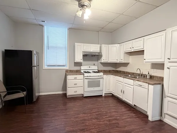 a white kitchen with granite countertop a stove top oven a sink dishwasher and a refrigerator with wooden floor