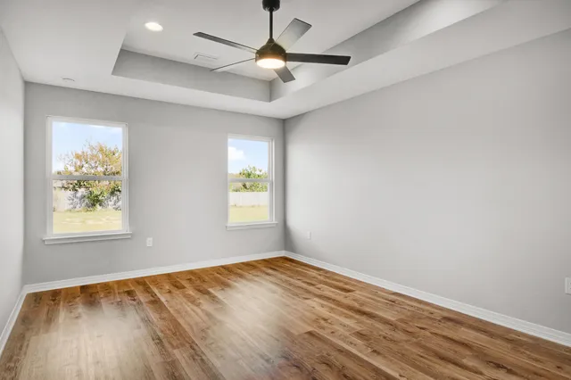 an empty room with wooden floor chandelier fan and windows