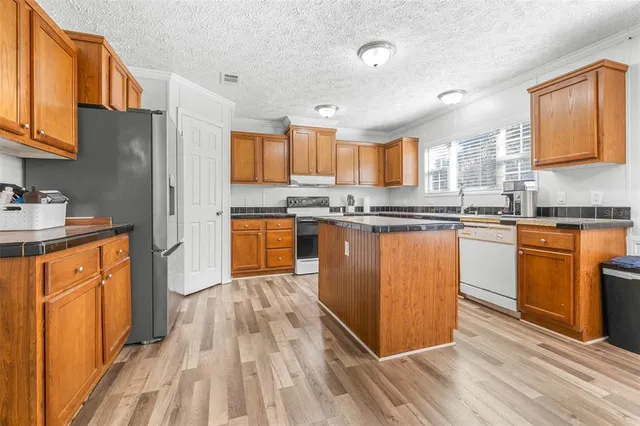 a kitchen with stainless steel appliances granite countertop wooden cabinets a sink dishwasher a stove and a refrigerator
