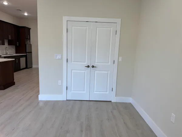 an empty room with wooden floor and kitchen view