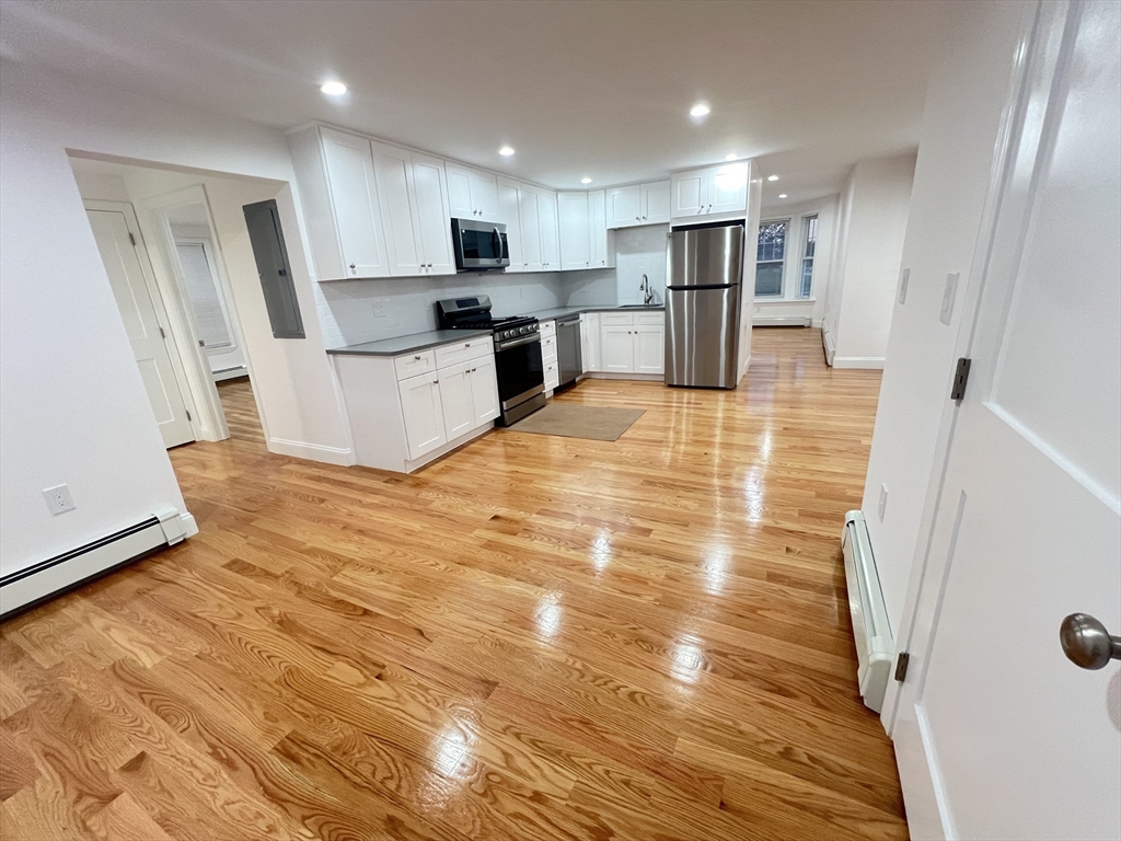 a large white kitchen with wooden floors and stainless steel appliances